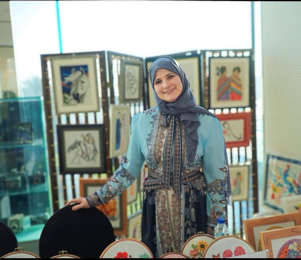 Suhair, the embroidery artist behind suhair_stitches, standing with her framed pieces at an exhibition